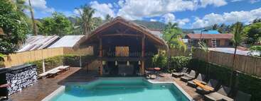 The image depicts a serene outdoor setting, featuring a pool and palm trees, with a large house in the background, evoking a sense of relaxation and tranquility. The atmosphere is peaceful and idyllic.