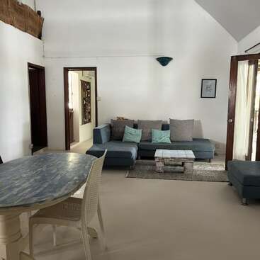 Dieser Raum hat ein modernes blaues Sektionssofa, einen rustikalen Couchtisch, einen Esstisch mit Stühlen, weiße Wände, eine hohe Decke und natürliches Sonnenlicht durch Glastüren.