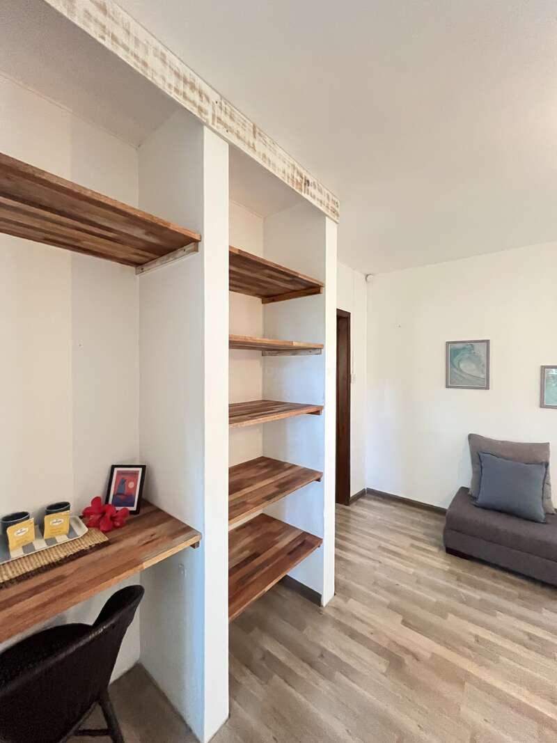 Dieses Bild zeigt einen gemütlichen Raum mit Holzregalen, einem kleinen Arbeitsbereich mit einem Stuhl, zwei gerahmten Bildern an der Wand und einem grauen gepolsterten Sitz.