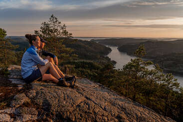 Un couple est assis au sommet d'une colline rocheuse, surplombant une vallée fluviale pittoresque remplie de forêts, profitant du coucher de soleil chaud et doré dans un silence paisible.