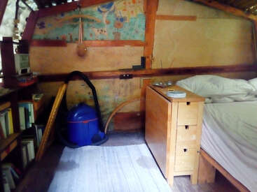The image depicts a cozy room with a bed, wooden furniture, and a blue vacuum cleaner, featuring a mural on the wall and a bookshelf in the background.