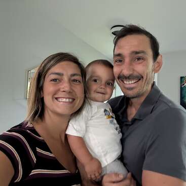 A happy family of three smiles for a selfie indoors. The woman holds the camera, the man holds a small child. Bright, cheerful atmosphere and close bonding.