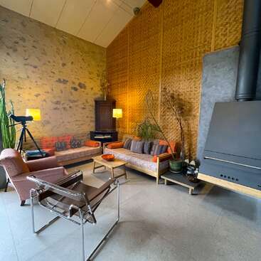 Ce salon confortable présente des tons terreux, un mobilier moderne, des murs texturés, un télescope, des plantes d'intérieur, un poêle à bois, un éclairage chaleureux et une atmosphère confortable et accueillante.