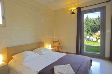 Cette chambre confortable dispose d'un lit double bien fait, de murs en bois, d'un éclairage doux, d'une grande fenêtre avec vue sur le jardin et d'une simple chaise dans le coin.