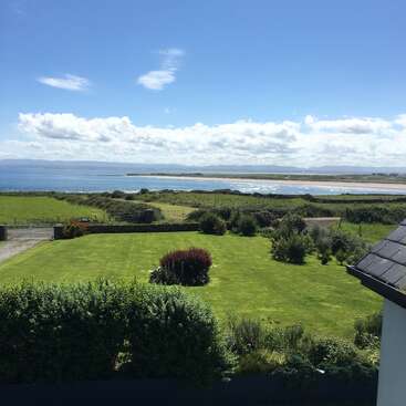The image depicts a serene coastal landscape featuring a lush green lawn, a tranquil body of water, and a blue sky with white clouds, evoking a sense of peacefulness.