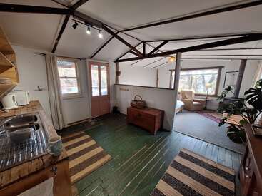 Cette cabane confortable dispose d'une cuisine rustique, de planchers en bois vert, de poutres apparentes, d'un coin salon confortable, de grandes fenêtres, d'une lumière naturelle et d'un décor accueillant.