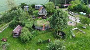 Dieses Luftbild zeigt ein ländliches Gehöft mit einzigartigen Häusern, üppigem Grün, Gärten, Bäumen, Sitzgelegenheiten im Freien, Gehwegen und einer ruhigen, friedlichen Atmosphäre inmitten von Feldern.