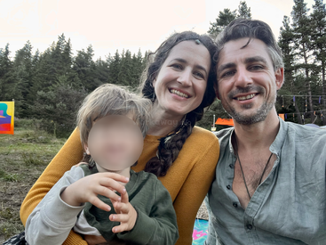 Une famille heureuse — un homme, une femme et un enfant — sourit ensemble en plein air. Entourés d'arbres et de décorations colorées, ils profitent d'une journée de détente dans la nature.