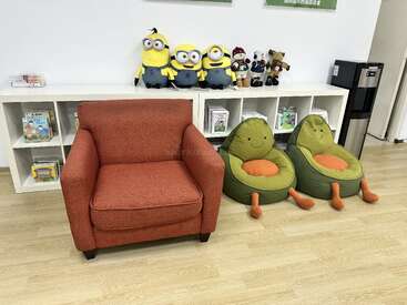 Este quarto aconchegante tem uma poltrona vermelha, dois pufes em forma de abacate, prateleiras brancas com livros, bichinhos de pelúcia e bonecos dos Minions, além de um bebedouro.