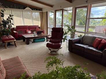 This cozy living room features large windows, plenty of natural light, red and brown couches, green plants, wooden beam ceiling, a coffee table, and scenic outdoor views.