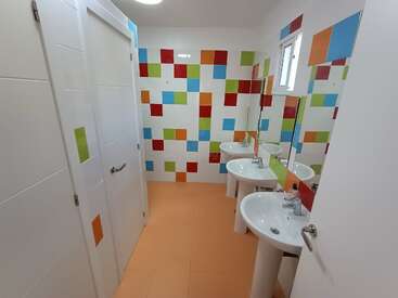 L'image représente une salle de bains aux murs et portes blancs, avec un carrelage vibrant sur le mur du fond, et trois lavabos surmontés de miroirs.
