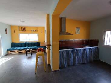 L'image représente un salon et une cuisine modernes avec des murs jaunes, un canapé bleu et un îlot de cuisine doté d'une hotte et d'un évier.