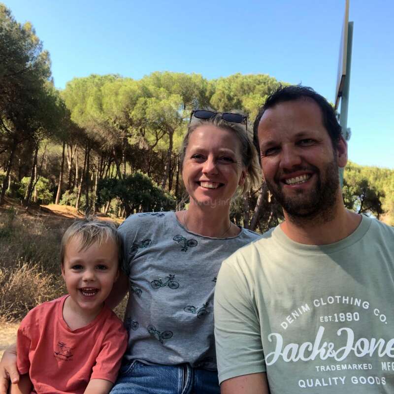 L'image représente une famille de trois personnes posant pour une photo dans une zone boisée, le père et la mère étant assis de part et d'autre de leur jeune enfant.