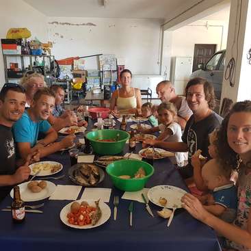 L'image représente un groupe de personnes réunies autour d'une table dans un garage, prenant un repas ensemble, avec une variété de nourriture et de boissons sur la table.