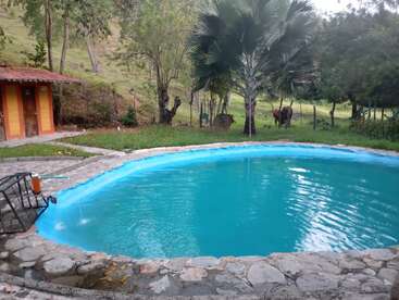 Das Bild zeigt einen ruhigen Garten mit einem kleinen, nierenförmigen Pool, der von einer Steinterrasse und üppigem Grün umgeben ist, mit einem kleinen Gebäude im Hintergrund.