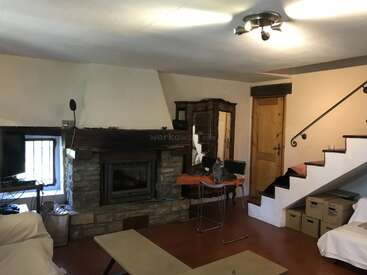 Ce salon confortable est doté d'une cheminée en pierre, de meubles en bois, d'un escalier avec des boîtes en dessous, d'une télévision et d'un mélange d'éléments rustiques et modernes.