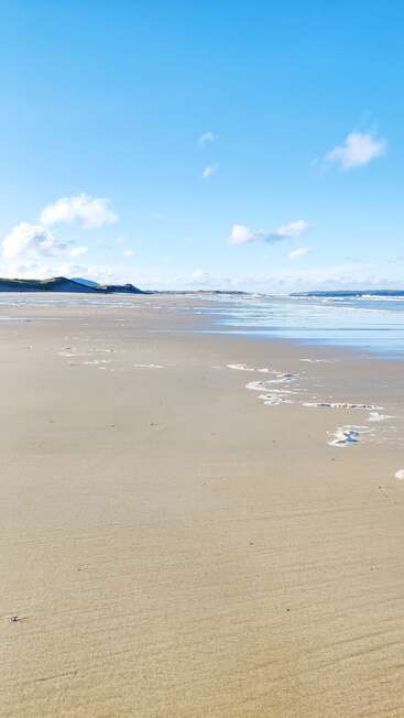 The image depicts a serene beach scene with a vast expanse of sand, gentle waves, and a clear blue sky, evoking a sense of tranquility and natural beauty.
