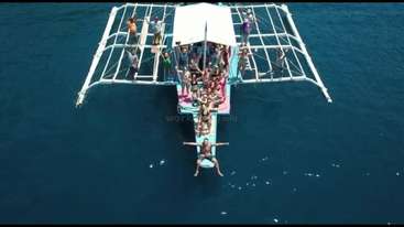 The image shows a group of people on a boat, with a large body of water in the background. The boat is likely a sailboat or a yacht. The people are enjoying themselves.