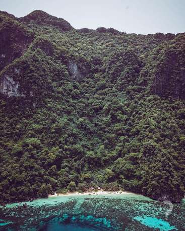 The image depicts a serene tropical landscape featuring a lush forested mountain, a sandy beach, and crystal-clear turquoise waters, evoking a sense of natural beauty and tranquility.