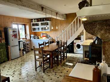Diese gemütliche Küche hat Holzwände, einen rustikalen Esstisch mit sechs Stühlen, freiliegende Deckenbalken, moderne Küchengeräte, eine Waschmaschine, Pendelleuchten und eine Treppe.