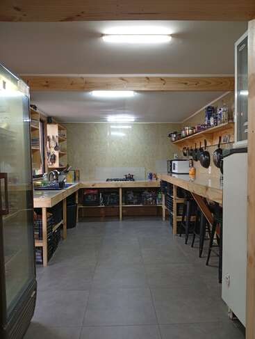 Cette photo montre une cuisine spacieuse et lumineuse, dotée de plans de travail en bois, d'étagères remplies d'ustensiles, de casseroles et de provisions. On y trouve des appareils électroménagers, des tabourets et des paniers de rangement bien organisés.