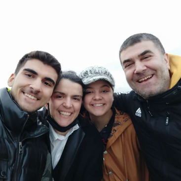 Cuatro personas, probablemente una familia, sonríen alegremente y posan juntas para un selfie al aire libre. Parecen alegres, abrigados con chaquetas y disfrutando de la compañía de los demás.