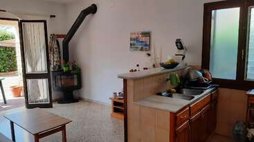 Esta acogedora cocina cuenta con armarios de madera, un fregadero doble y secado de platos. Hay una estufa de leña, puerta abierta, luz natural y una pequeña mesa de café.