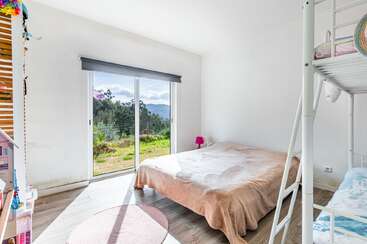 Este quarto bem iluminado e arejado tem uma janela grande com uma bela vista para o exterior, uma cama de casal, beliches, piso de madeira e uma decoração minimalista e alegre, que convida ao relaxamento.