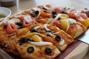The image depicts a pizza with toppings, featuring a circular base, toppings, and a crust, set against a background of a table or countertop. The pizza is cut into slices.