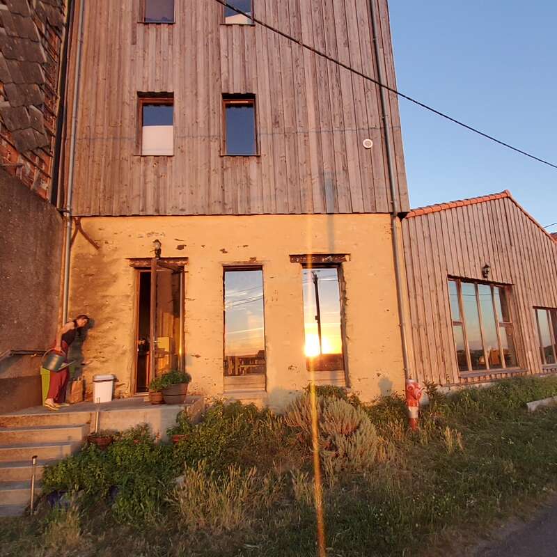 L'image montre une maison avec une grande cour et une allée, comprenant un bâtiment de deux étages avec un toit à deux versants et un porche couvert. La maison est située dans une zone suburbaine.