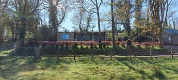 Das Bild zeigt eine ruhige Szene eines Hauses mit einem großen Garten, einer von Bäumen gesäumten Auffahrt und einem gepflegten Rasen, umgeben von einer ruhigen und friedlichen Umgebung.