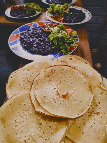 Plusieurs assiettes sont disposées sur une table en bois, chacune contenant des haricots noirs, de la salade verte et des tomates. Au premier plan, on aperçoit une pile de tortillas.