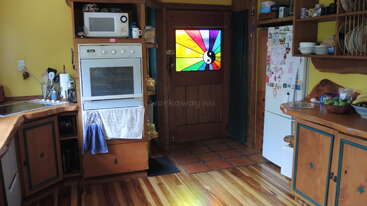 This cozy kitchen features wooden cabinets, a microwave, oven, and fridge adorned with magnets. A colorful stained-glass door adds vibrant charm to the warm, inviting space.
