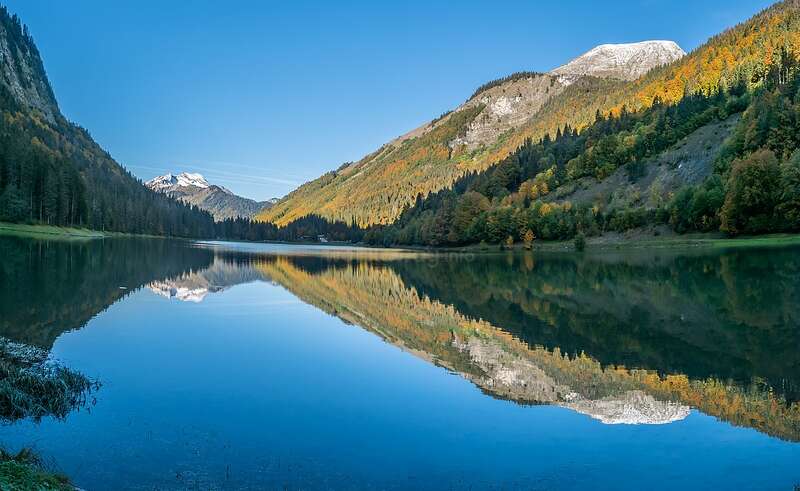 L'image représente un paysage serein avec un lac, entouré d'arbres et de montagnes, avec un ciel clair et des eaux calmes, évoquant un sentiment de paix et de tranquillité.