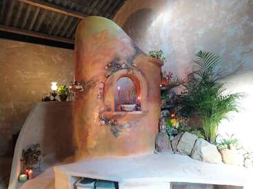 A imagem mostra um cômodo sereno com uma parede arredondada exclusiva com uma janela em arco, adornada com plantas e velas, criando um ambiente tranquilo.