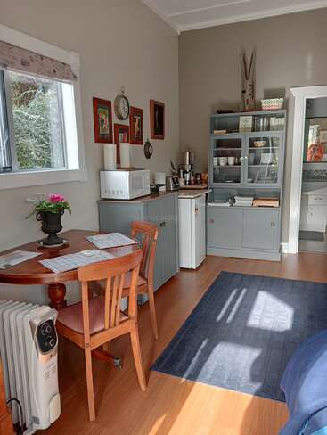 L'espace cuisine-salle à manger, confortable et ensoleillé, est doté de sols en bois, d'une petite table ronde avec des chaises, d'un tapis bleu, d'appareils de cuisine, d'œuvres d'art murales et d'une fenêtre.