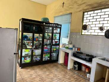 Essa foto mostra uma cozinha arrumada com um armário de vidro cheio de pratos, um fogão, utensílios pendurados, uma geladeira, piso de azulejo e paredes amarelas brilhantes.