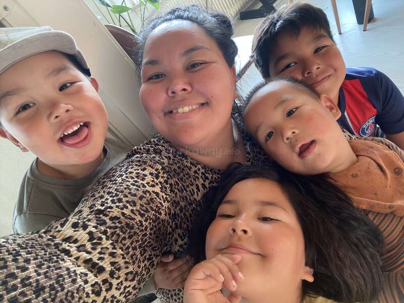 Eine Frau und vier Kinder lächeln und posieren eng beieinander für ein fröhliches, verspieltes Selfie in einem Haus. Sie wirken fröhlich und zufrieden und genießen ihre gemeinsame Zeit.