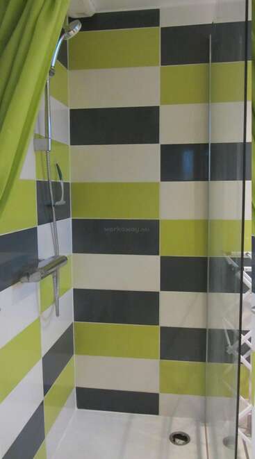 Esta imagen muestra una ducha moderna con un patrón de azulejos a cuadros en verde, blanco y gris oscuro. Hay una alcachofa de ducha, una cortina y una mampara de cristal.