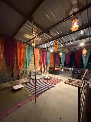 A cozy, traditional room with colorful drapes, patterned cushions on the floor, low tables, hanging lanterns, and warm lighting, creating a charming, inviting atmosphere for relaxation.