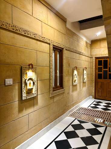 This image shows a well-lit corridor with yellow stone walls, intricate carved decorations, window, wooden door, black-and-white diamond patterned floor, and beautiful ornamental wall lights.