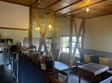 Este acogedor café cuenta con vigas de madera, una cálida iluminación, tarros llenos de ingredientes, una pequeña zona de cocina y cómodos asientos junto a una ventana con suaves cojines.
