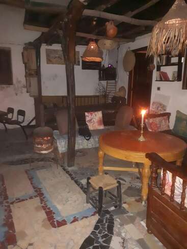 The image depicts a cozy living room with a wooden table, candle, and couch, featuring a unique mosaic tile floor and eclectic decor, including a fireplace and hanging lights.