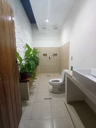 Dieses Bild zeigt ein modernes Badezimmer mit beigen Fliesen, einer weißen Toilette, einem großen rechteckigen Waschbecken, grünen Topfpflanzen und einer minimalistischen Einrichtung, die eine frische Atmosphäre schafft.