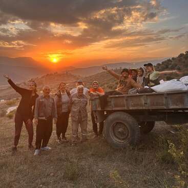 Das Bild zeigt eine Gruppe von Menschen, die bei Sonnenuntergang auf einem Hügel für ein Foto posieren, mit einem Lastwagen in der Nähe und einer malerischen Landschaft im Hintergrund.