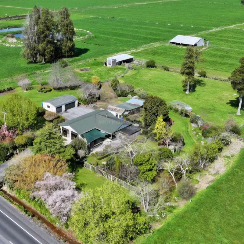 Vista aérea de uma propriedade rural com uma casa de telhado verde, vários anexos, jardins exuberantes, áreas cercadas e vastos terrenos agrícolas ao redor. Um ambiente tranquilo e pitoresco.