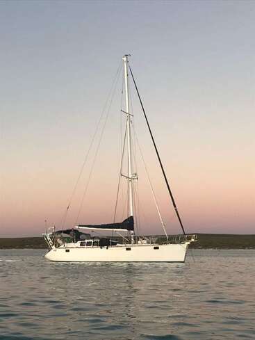 The image depicts a serene scene of a white sailboat floating on calm water, set against a vibrant sunset sky with hues of pink and orange.