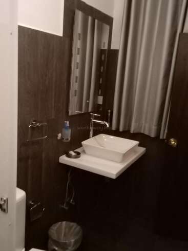The image depicts a bathroom with a white sink, mirror, and trash can, featuring dark wood paneling on the walls and a white door.