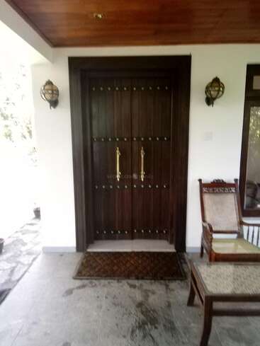 The image depicts a serene entryway with a dark wood door, white walls, and a wooden ceiling, featuring a chair and table on the right side.