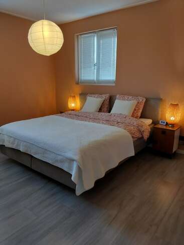 Une chambre confortable aux murs orange comprend un lit double, des oreillers à motifs, deux tables de chevet avec des lampes en osier, une lanterne en papier et une fenêtre avec des stores.